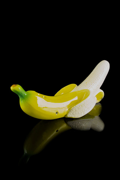 Glass banana-shaped cannabis pipe with yellow and green hues, reflecting on a black surface.