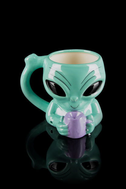 Green alien-shaped ceramic mug holding a purple cannabis bud, reflected on a black surface.