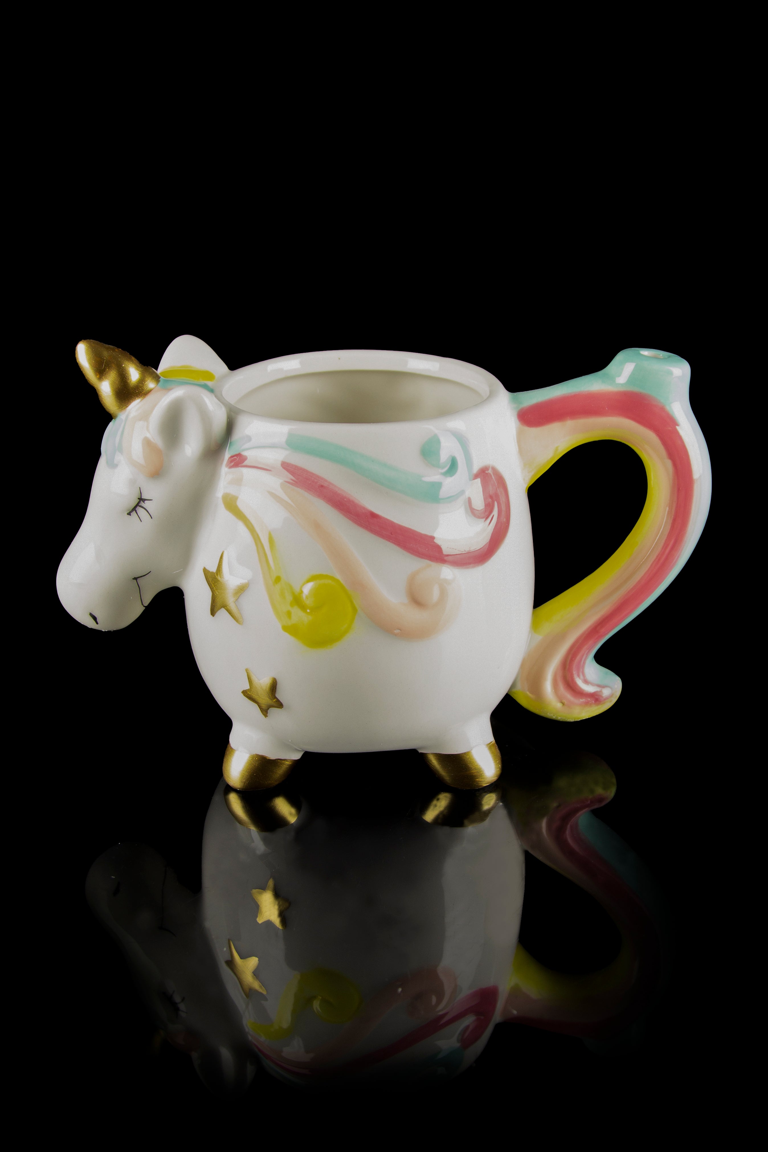 White ceramic unicorn-shaped pipe with gold hooves and a rainbow-colored tail, reflecting on a dark surface.