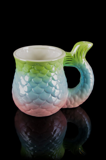 A colorful, mermaid-scale patterned glass pipe with a sculpted fin handle, reflected on a black surface.