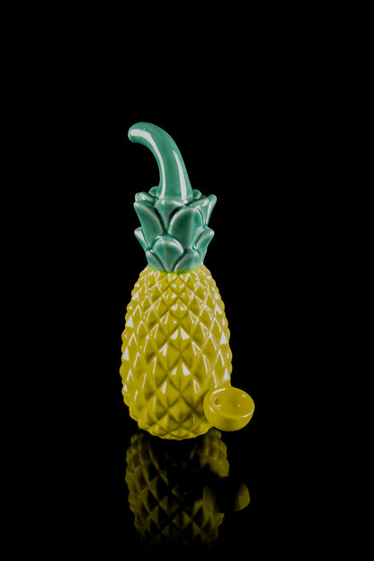 A glass pineapple-shaped water pipe with a green stem and base, reflected on a black surface.