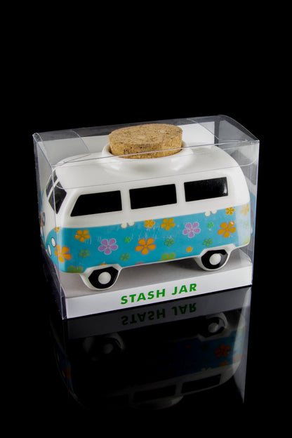 A turquoise Volkswagen van-shaped “stash jar” encased in a clear plastic container, reflecting on a glossy black surface.