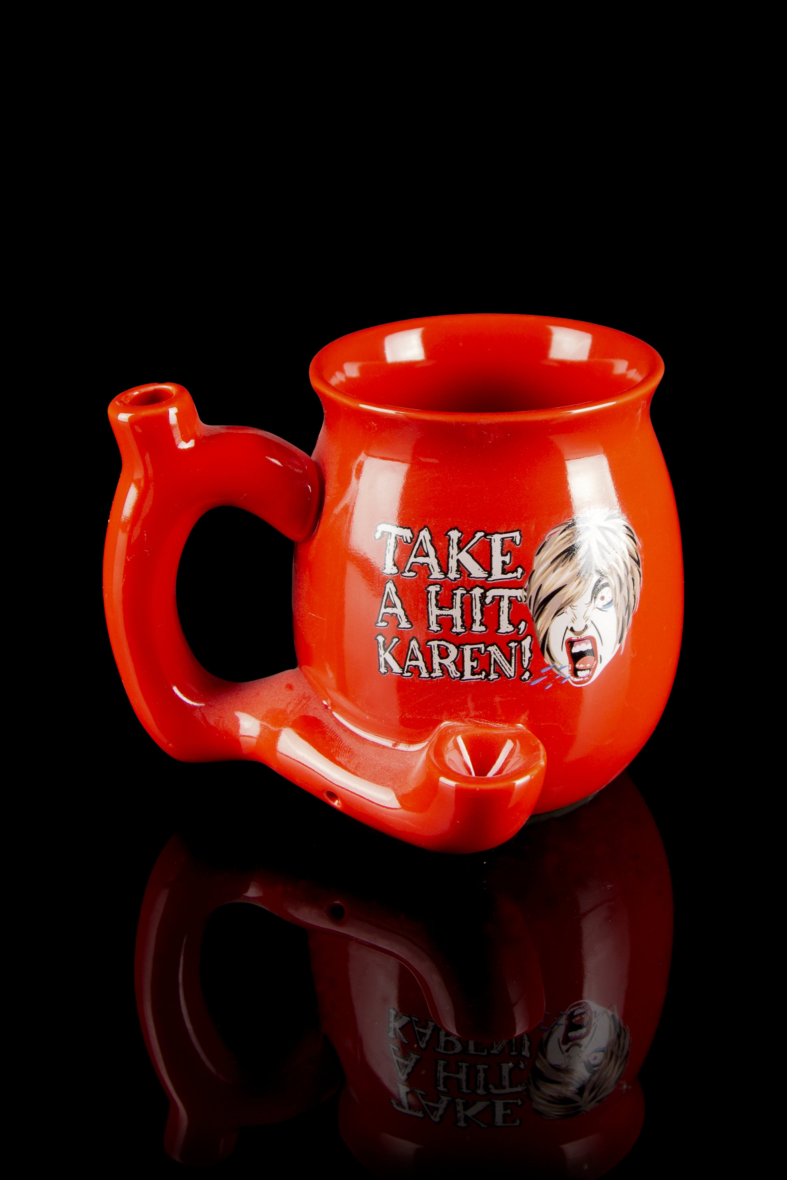 Red ceramic water pipe with the phrase “Take a hit Karen!” and a cartoon face etched on the side, displayed on a reflective surface against a black background.