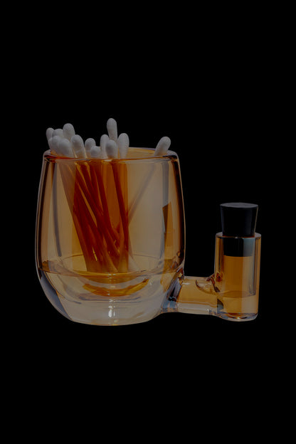 Amber glass dab rig with cotton swabs inside and a small concentrate container attached.