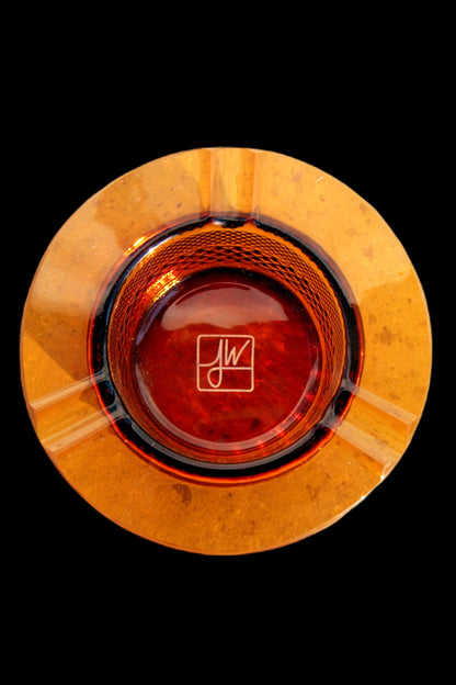 Overhead view of an orange glass ashtray with a signature etched in the center.