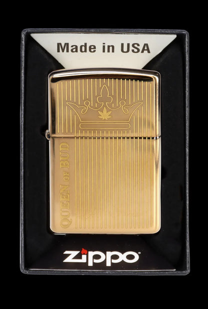 Gold Zippo lighter with a cannabis leaf crown design and “Queen of Bud” engraved on the side, displayed in a black plastic case.