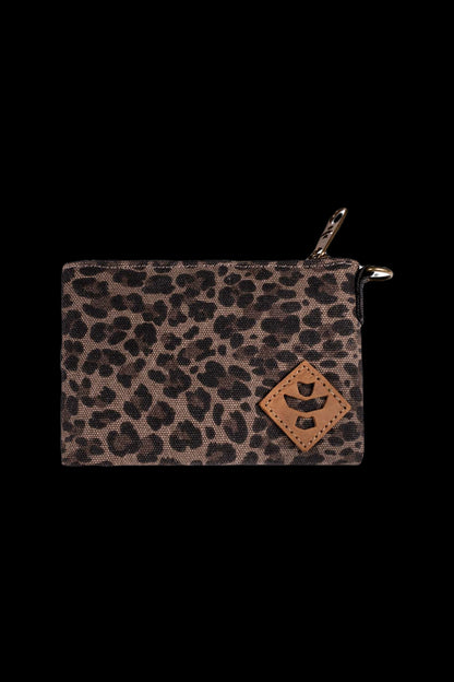 Close-up front view of the Revelry Supply Smell Proof Zippered Small Stash Bag - The Mini Broker showing a leopard-print fabric, leather diamond patch, and top zipper against a black background.