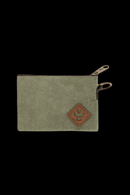 Top-down close crop of the Revelry Supply Smell Proof Zippered Small Stash Bag - The Mini Broker showing an olive canvas corner, leather diamond patch, and brass zipper pulls.