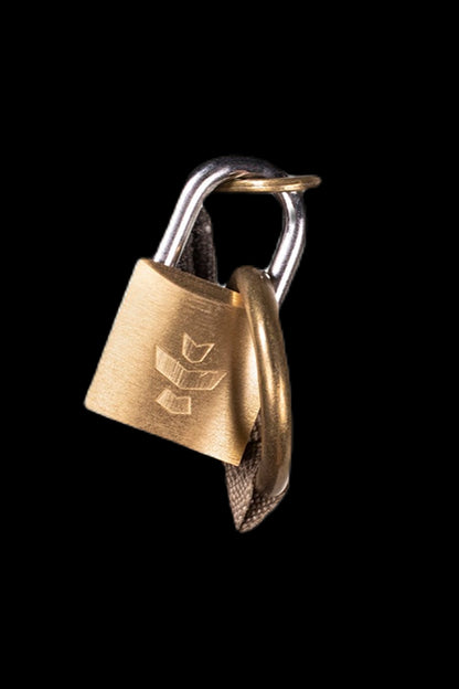 Gold padlock with a cannabis leaf imprint hanging from a woven strap, isolated on black.