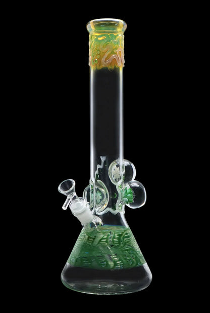 Front view of the Smoke Cartel Mushroom Marble Water Pipe - 18 in. showing a clear glass beaker with green textured base, decorative mushroom marbles, and a yellow-green flared mouthpiece against a black background