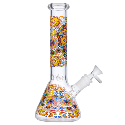 Side view of the Smoke Cartel Skull Beaker Bong - 10 in. showing a clear glass beaker with colorful yellow, orange, and blue floral skull motifs wrapping the neck and base.