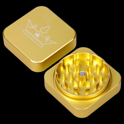 Gold cannabis grinder with a crown and leaf design, open to reveal the grinding teeth.