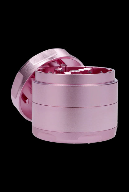 Pink four-piece cannabis grinder with open lid, isolated on a black background.