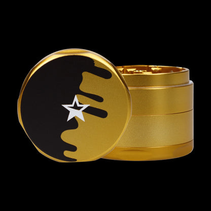 Close-up front view of the Famous Design-Surrender Aluminum 3 Stage Grinder-Gold showing its gold stacked body and black-top with a white star emblem.