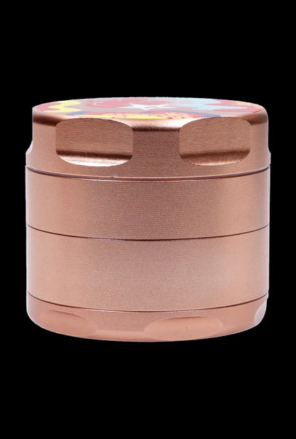 Close-up front view of the rose gold Famous Design-Papaya Aluminum 3 Stage Grinder-Rose Gold showing stacked textured chambers and a colorful patterned lid against a black background