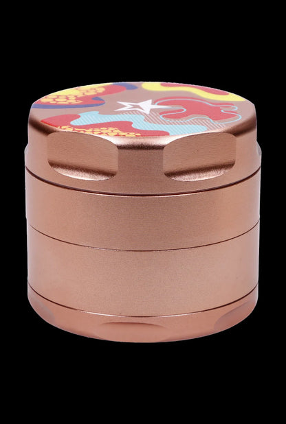 Close-up front view of the Famous Design-Papaya Aluminum 3 Stage Grinder-Rose Gold showing its cylindrical, three-tiered rose gold body and colorful patterned lid.