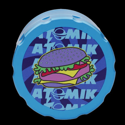 A circular, translucent blue silicone cap with a cartoon hamburger and the text "ATOMIK" repeated around it. 