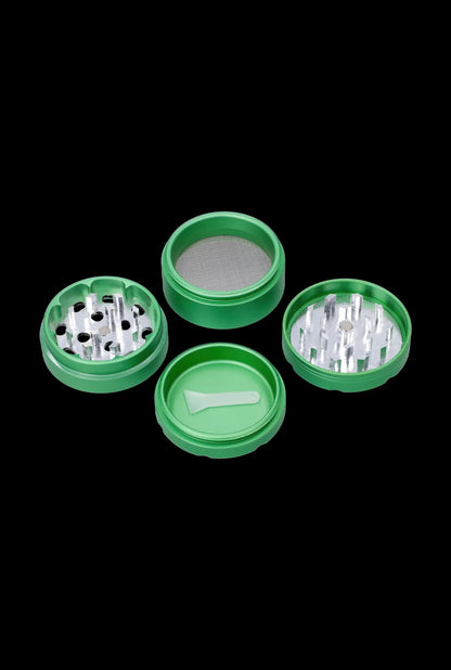 Top-down view of the disassembled Cabana Cannabis Co. 3-Stage Grinder Parasol Green showing four bright green circular sections and a small scraping tool against a black background