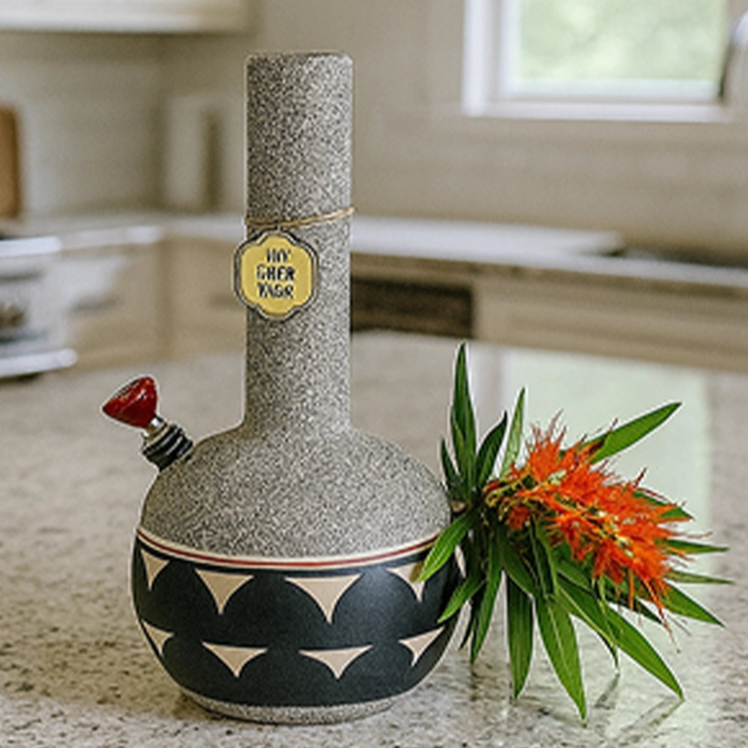 Side view of the textured, patterned My Bud Vase Bong - Coyote sitting on a kitchen countertop next to orange flowers.