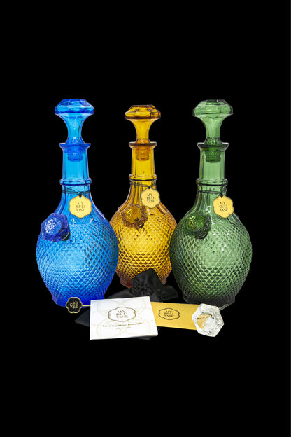 Three intricately patterned glass cannabis water pipes in blue, amber, and green stand before black cards displaying the brand “My Bud Vase.”