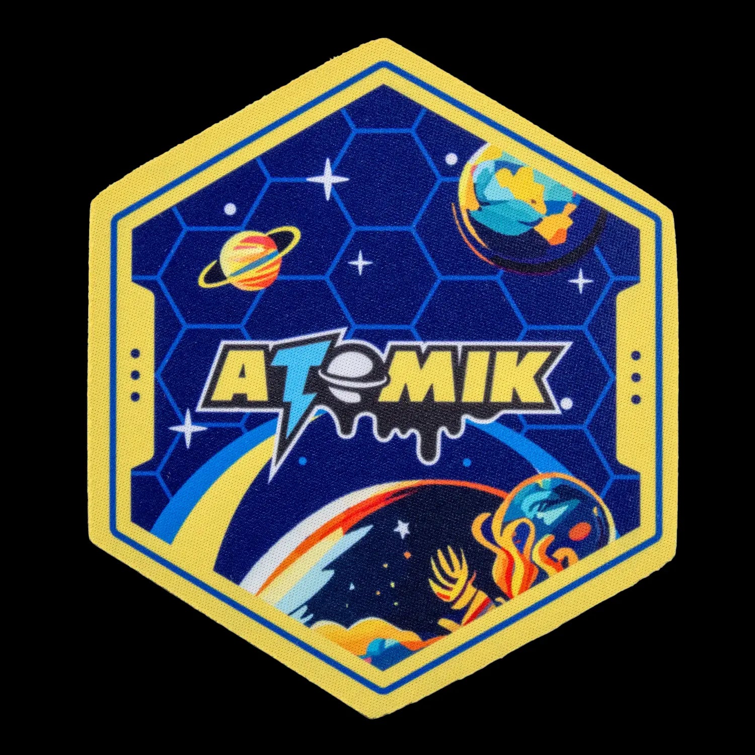 Hexagonal patch with a space theme, featuring the brand name “ATOMIK” in bold lettering over a starry blue background with planetary illustrations.