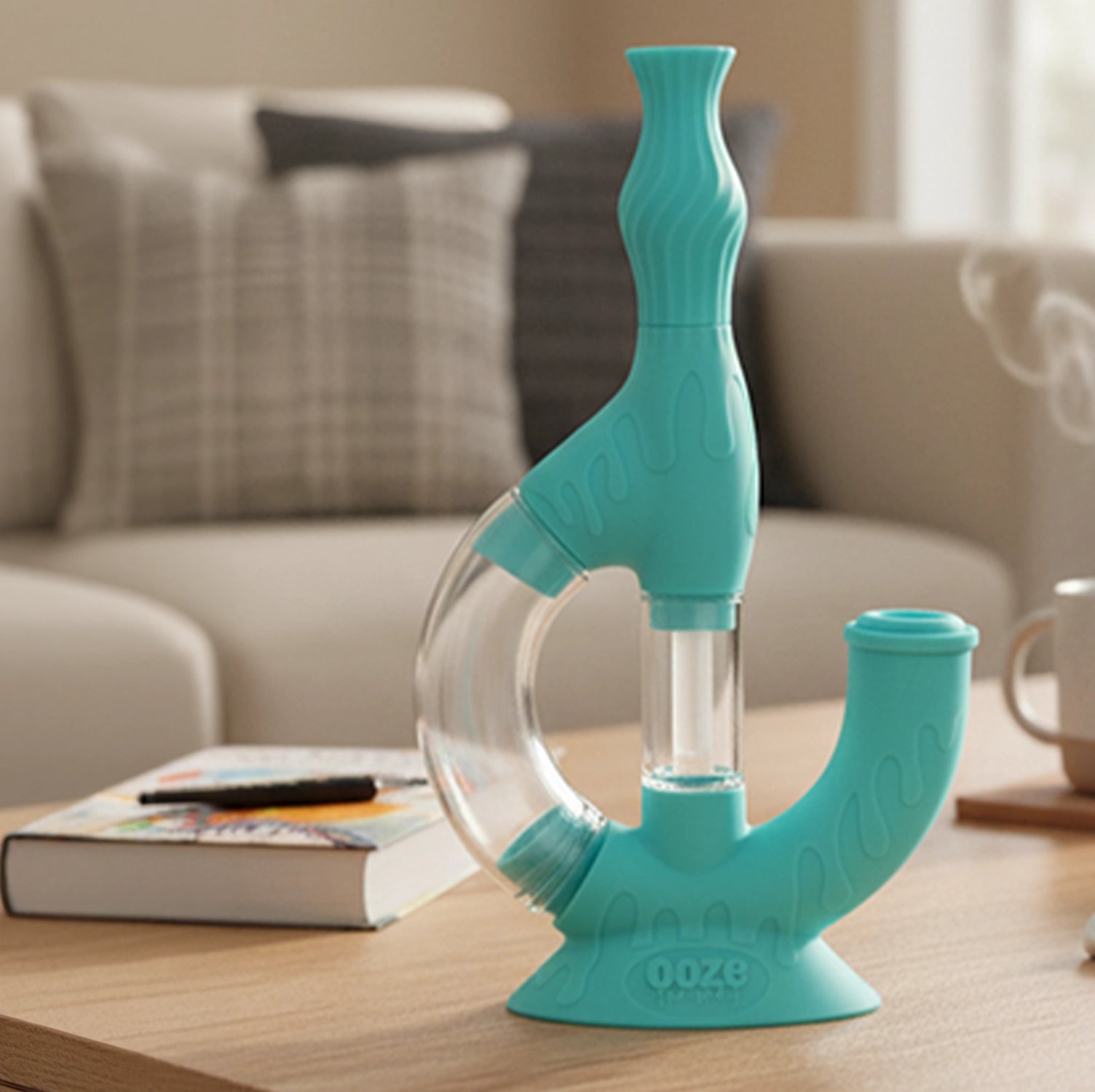 Close-up, three-quarter view of a turquoise Ooze Echo Silicone Bong on a wooden table with a blurred sofa and book in background