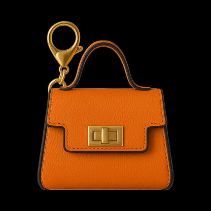 Close-up front view of the orange Hermione Penjamin Pursejamin Vaporizer showing its textured leather flap, gold clasp, top handle and lobster clasp against a black background