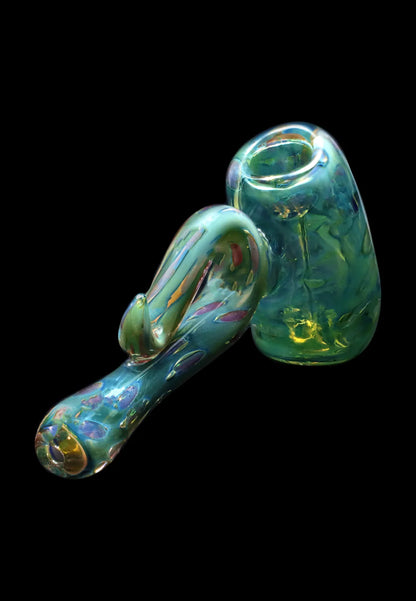 Angled close-up of the Smoke Cartel Gold Fume Bubble Trap Hammer Bubbler - 6 in., showing iridescent green-blue glass with swirling gold and purple highlights against a black background