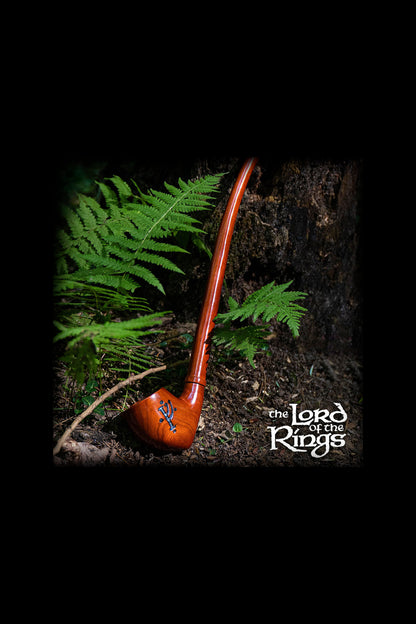A wooden smoking pipe rests on moss and ferns, evoking a natural, earthy aesthetic, with "The Lord of the Rings" logo subtly displayed.