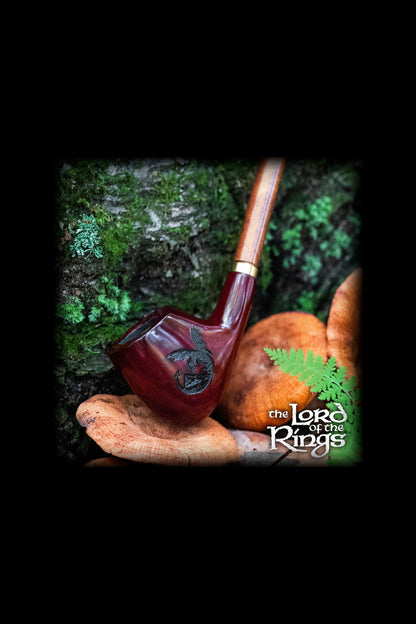 A carved wooden pipe rests in a hand against a blurred green forest backdrop, with "The Lord of the Rings" logo at the bottom.