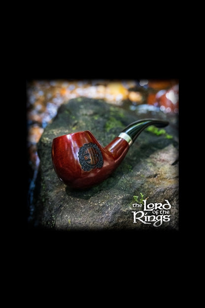 A carved wooden pipe rests on a mossy surface, evoking a fantasy aesthetic with "The Lord of the Rings" logo at the bottom.