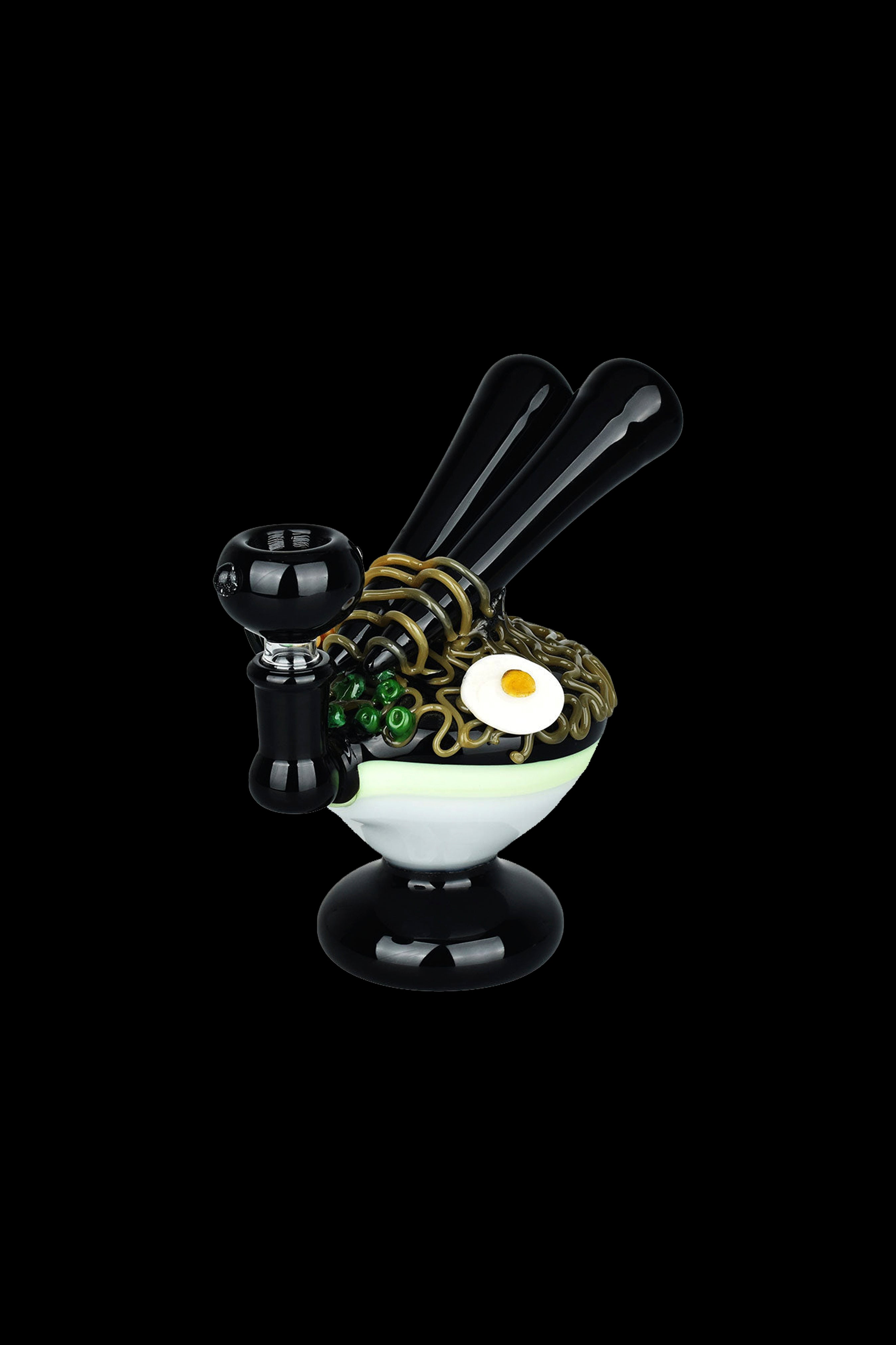 A sculptural glass rig resembling a cartoon character with a bowl piece as a head, coils as hair, and a fried egg detail, set against a black background.