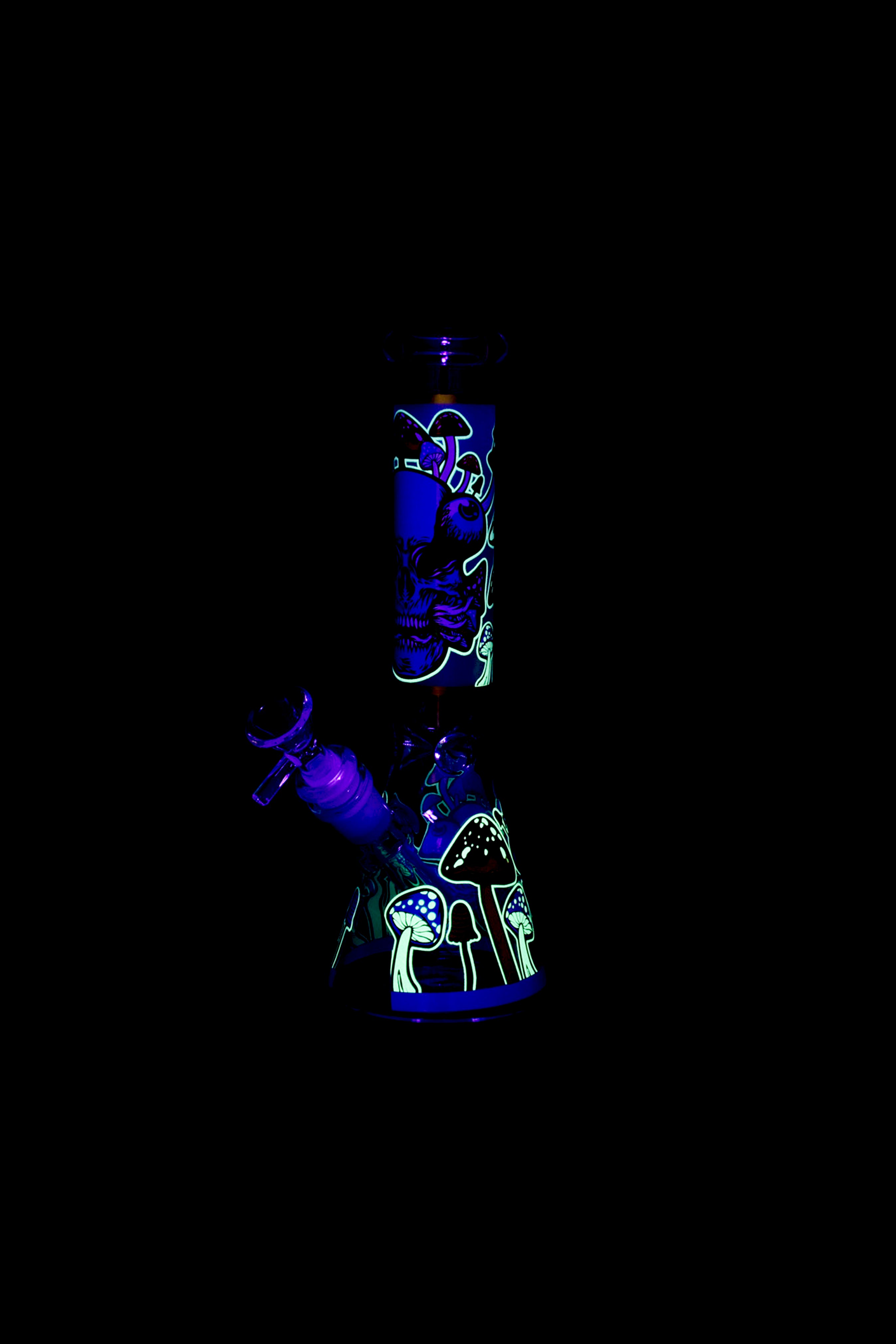 Glowing glass water pipe with psychedelic mushroom and face designs against a black background.