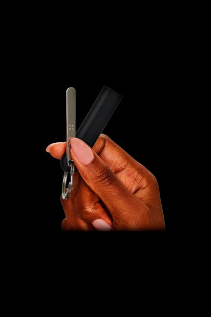 Hand holding a black Pax vaporizer pen with a key ring attached, against a black background.