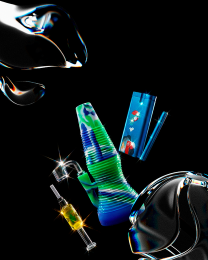 Angled view of the orange Smoke Cartel Rigid Silicone Mini Dab Rig set against a black background, showing its ribbed, green-and-blue silicone body alongside a glass nail, torch, and stylized reflective props.