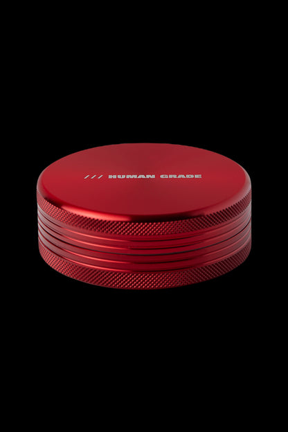 Red four-piece cannabis grinder with “HUMAN GRADE” engraved on top.