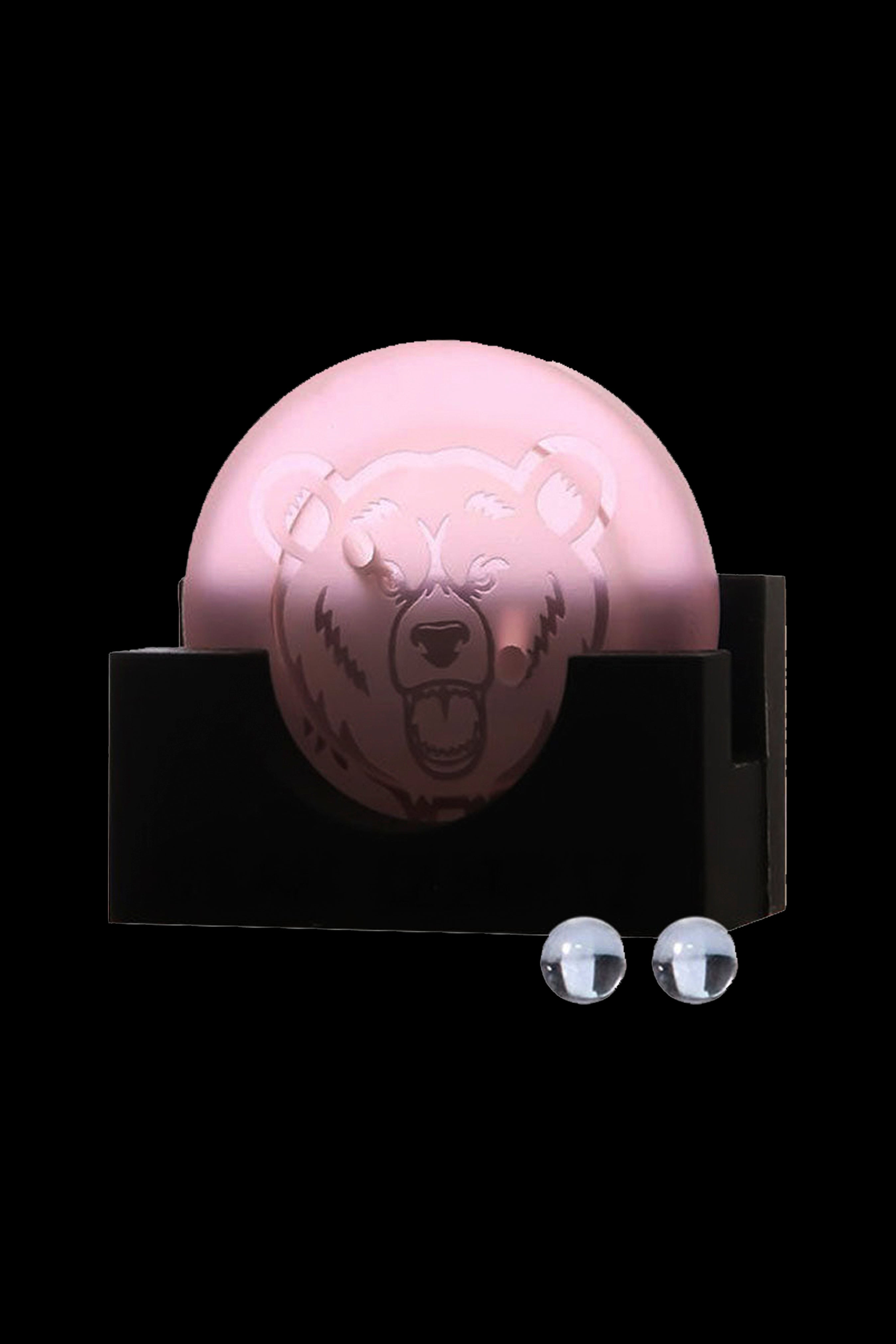 Pink bear-shaped smoking device with two glass marbles on a black surface.
