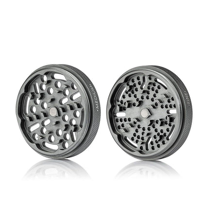 Front-facing studio shot of two metallic RYOT GR8TR Solid Body Grinder halves with textured edges and patterned grinding holes reflected on a white surface