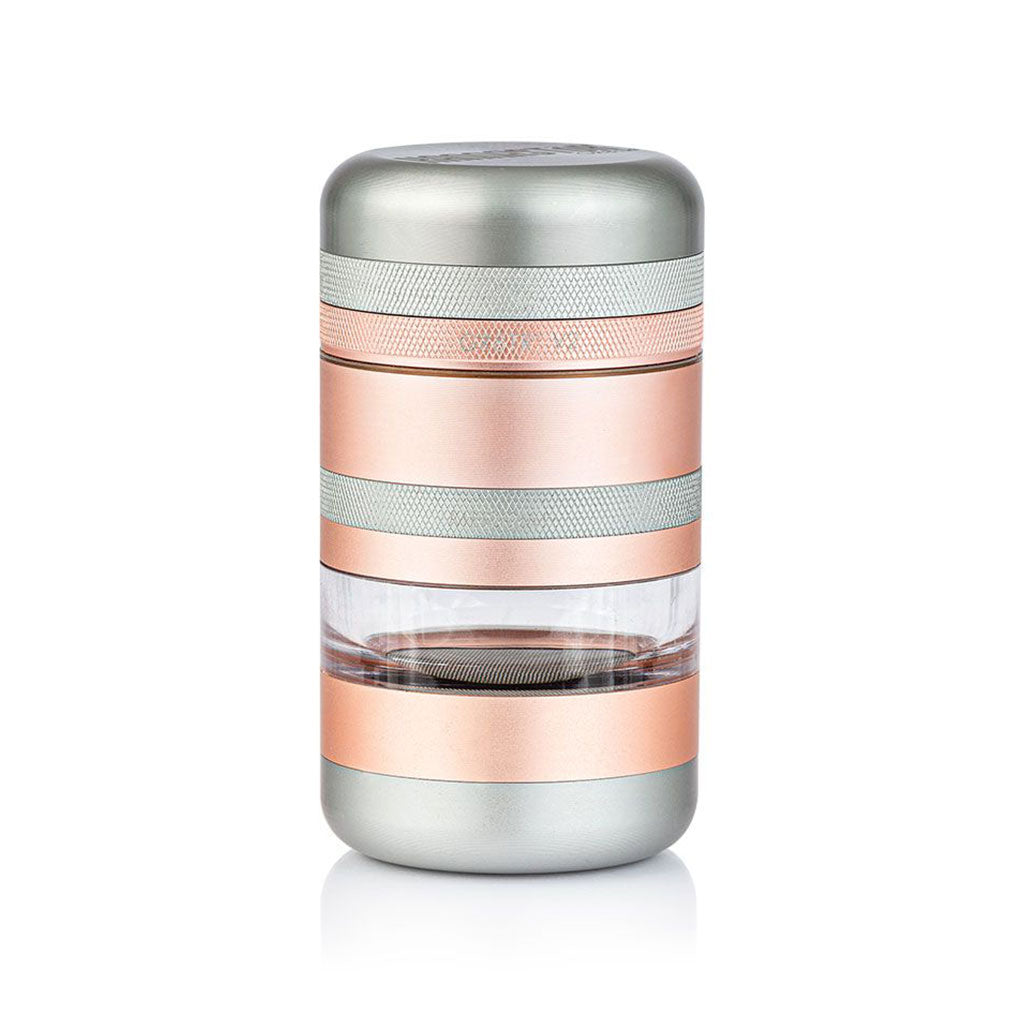 Studio-lit front view of the RYOT GR8TR Jar Body Grinder showing its stacked silver and rose-gold metal bands with a clear middle chamber.