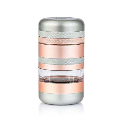 Studio-lit front view of the RYOT GR8TR Jar Body Grinder showing its stacked silver and rose-gold metal bands with a clear middle chamber.