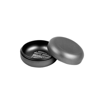 Angled view of the matte black RYOT GR8TR Jar Body Grinder with its rounded lid removed to reveal a shallow inner chamber and visible white text on the base