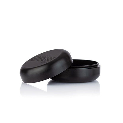 Three-quarter view of the matte black RYOT GR8TR Solid Body Grinder with its lid tilted beside the base on a reflective white surface