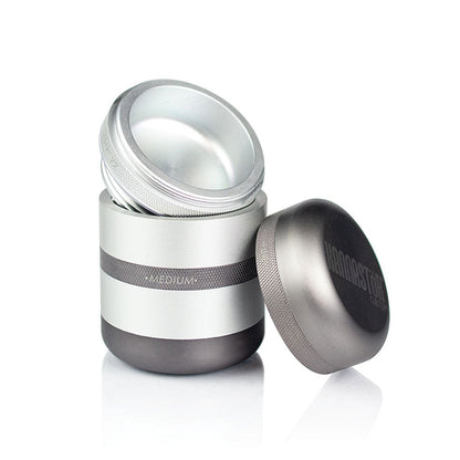 Angled front view of the matte silver RYOT GR8TR Solid Body Grinder with its lid removed and placed beside the cylindrical, two-tone grinding chamber.