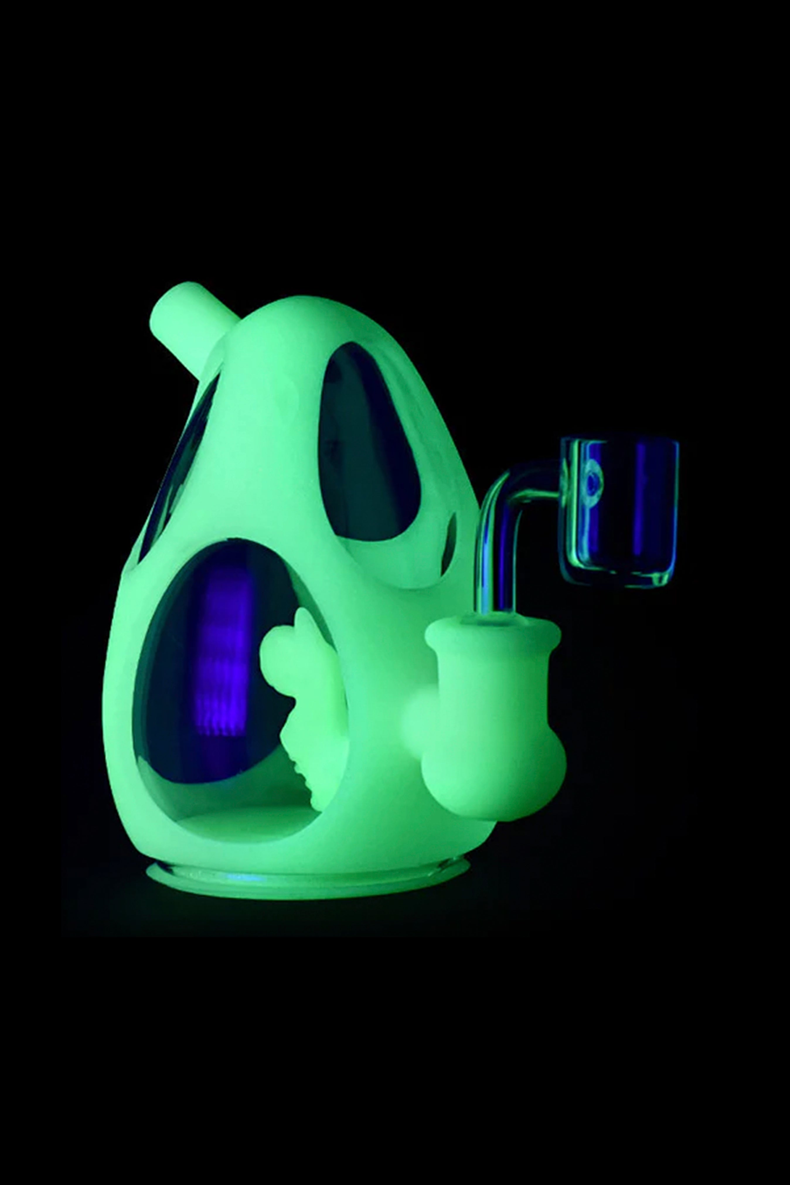 Glowing green glass water pipe and accompanying tools against a black background.