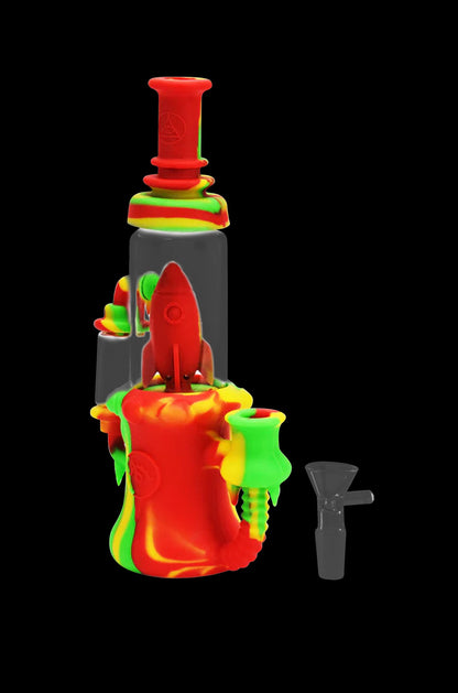 Red and green silicone water pipe with a rocket ship design, and a glass downstem beside it.