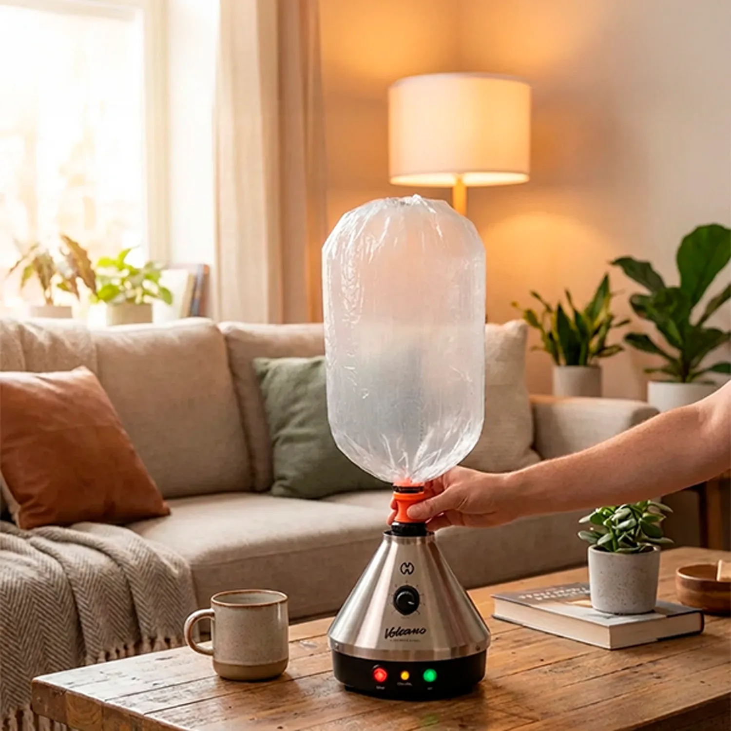 Handheld shot showing the stainless-steel Storz & Bickel Volcano Classic on a coffee table with its clear balloon bag attached, warm lamp light and sofa in the background