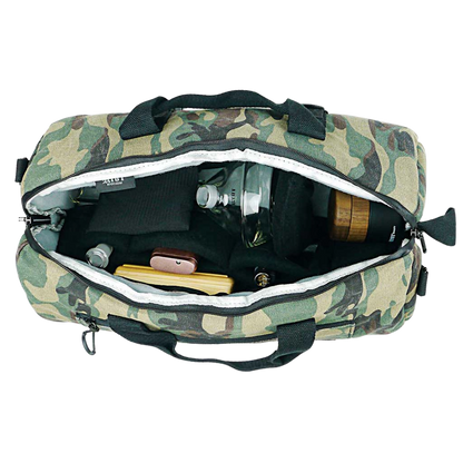 Top-down view into a camo RYOT Pro-Duffle Carbon Series Smell-Proof Bag with its zipper open showing padded black interior pockets and small glass and wooden items inside.