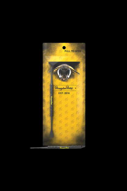 Top-down view of the Honeybee Herb Stainless Steel Dabber - V1 resting against its yellow branded card featuring a close-up bee illustration.
