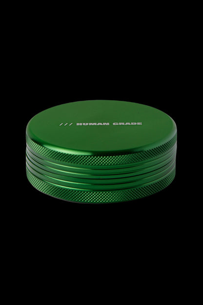 Green metal cannabis grinder with "HUMAN GRADE" text.