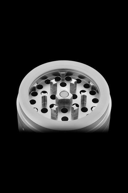 Silver cannabis grinder with visible teeth and chambers against a black background.